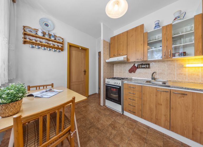 A kitchen in a 3-room apartment with a kitchenette, wood decor, and a dining table with chairs.