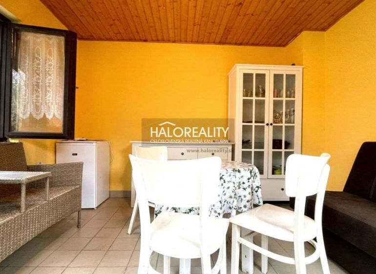 Interior of a garden with a white dresser, table, and wicker furniture, yellow walls.