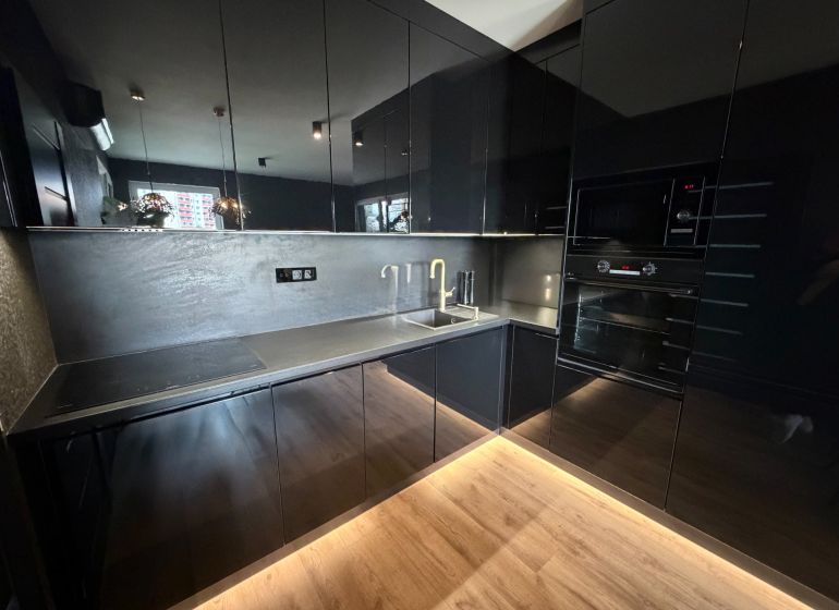 Black kitchen in a 2-room apartment with a wooden decor floor.