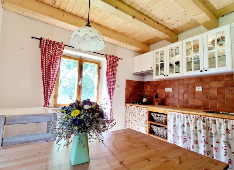 A kitchen in a cottage with a wooden ceiling, a floor with a wooden decor, flowers on the table.
