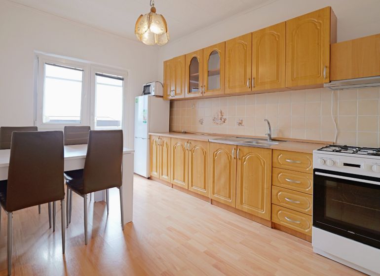 A kitchen in a 3-room apartment with a kitchen unit, dining table, and a floor with a wooden decor.