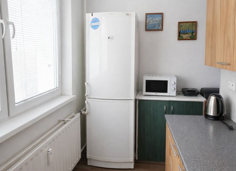 Kitchen in a 2-room apartment with a refrigerator and kitchen unit, floor with wooden decor.