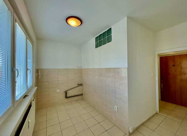 An empty kitchen area with light tiles in a studio apartment.