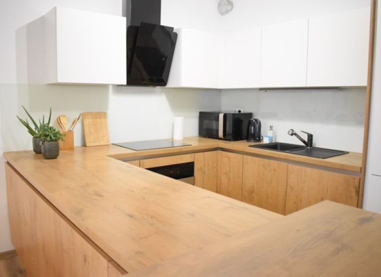 Kitchen in a 2-room apartment with a counter, white cabinet, wooden decor flooring.
