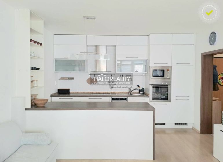 A kitchen with white cabinets and built-in appliances in a 2-room apartment, with a wood-patterned floor.
