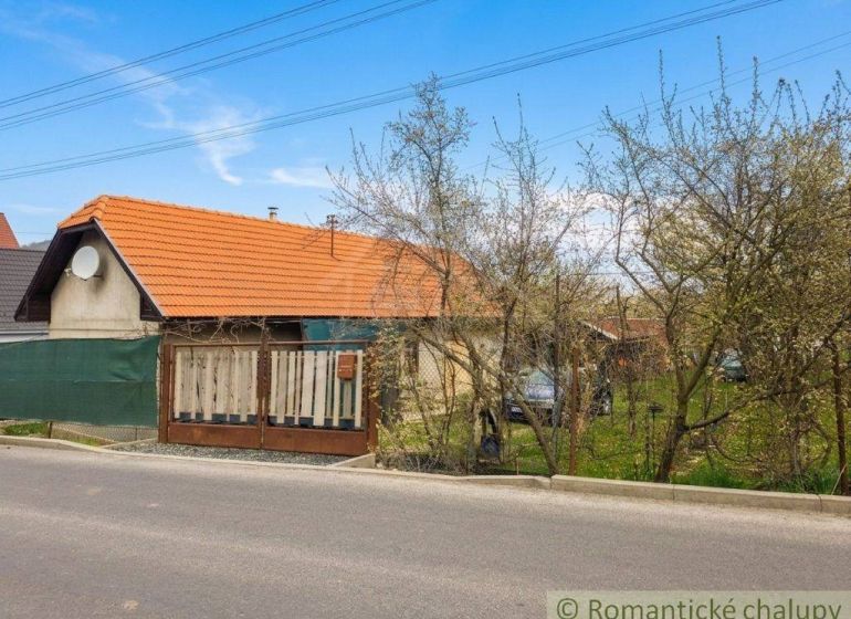 A family house in Stožok with a red roof, a fence, and a garden near the road.