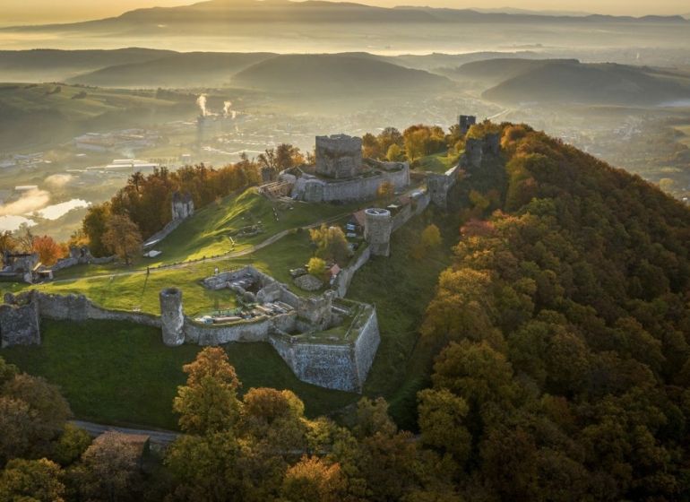A castle on a hill surrounded by autumn-colored forests in the area of Veľký Šariš.