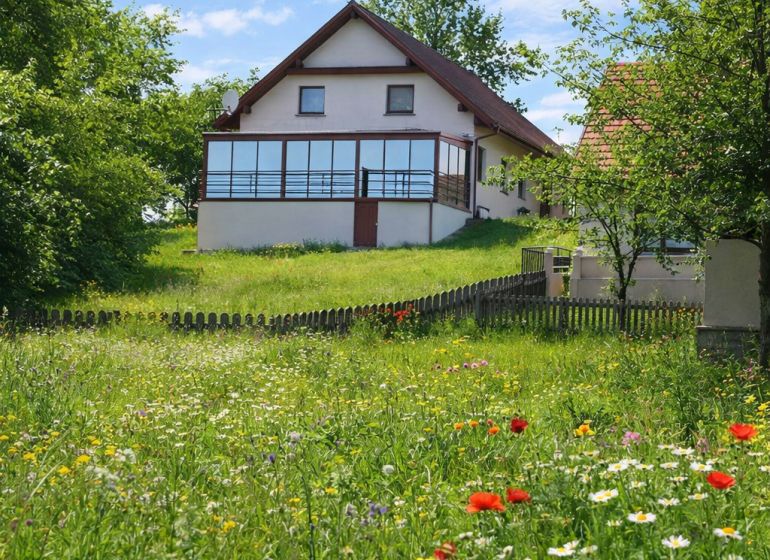 A family house in Oravská Lesná bordered by a flowery meadow and a wooden fence.