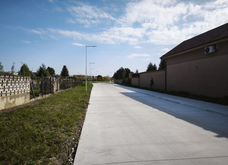 Concrete sidewalk in Čierny Brod for residential plots next to grassy and fenced areas.