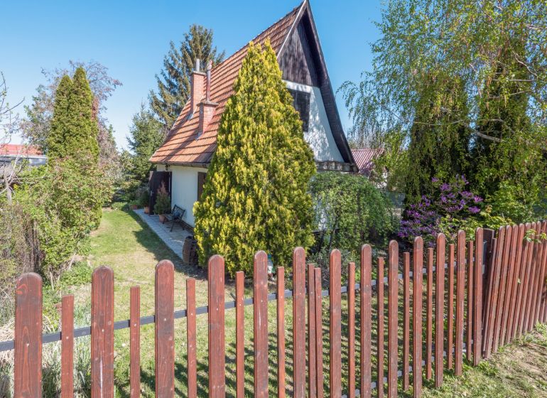 A cottage in Nitra surrounded by greenery with a wooden fence and a garden.