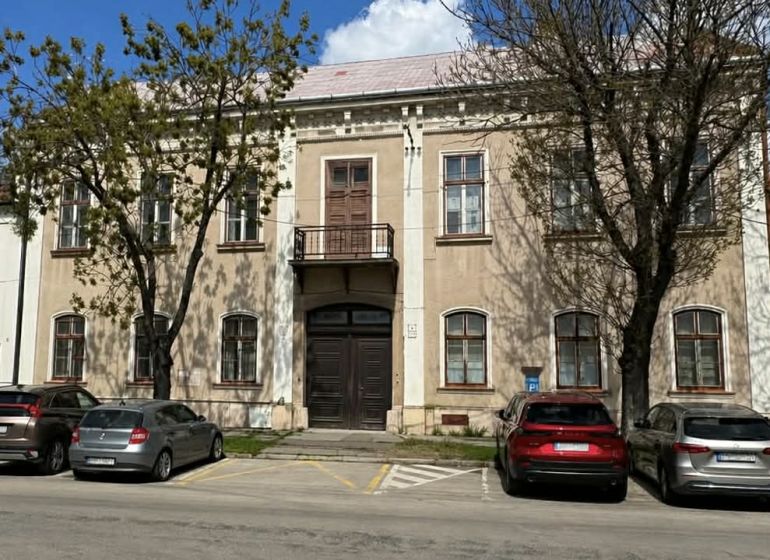 A building in Komárno used for special properties, surrounded by trees and a parking lot.