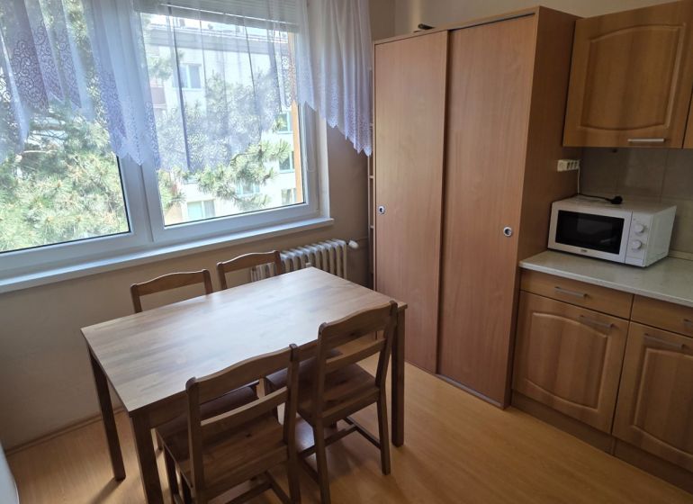 A kitchen in a one-room apartment with a wood-patterned floor, table, and cabinets.
