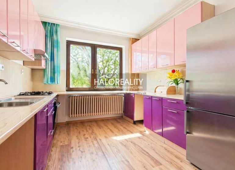 A kitchen with purple and pink cabinets, a wooden-patterned floor, a large window.