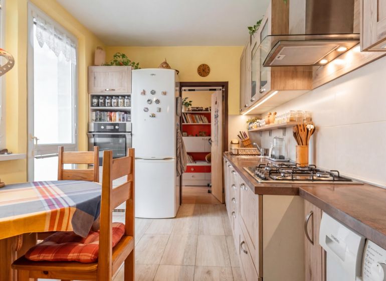 A kitchen in light shades with built-in appliances, a dining table, and a decorated wall.