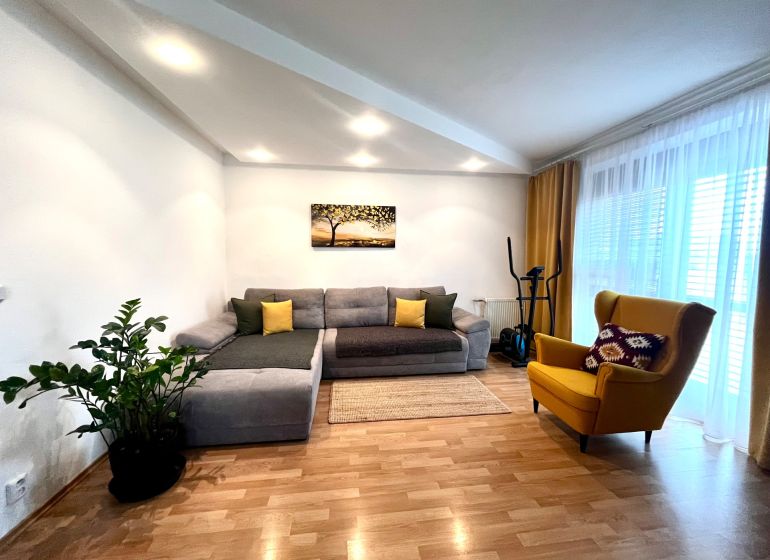 Living room of a three-room apartment with a wooden decor floor, gray sofa, and yellow armchair.