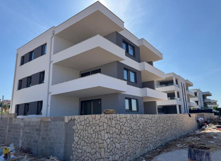 A recreational apartment in Novalja, a three-story building with a stone fence and spacious balconies.