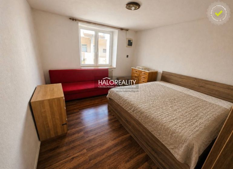 A bedroom with wooden decor, a bed, a red sofa, and a window in a family house.