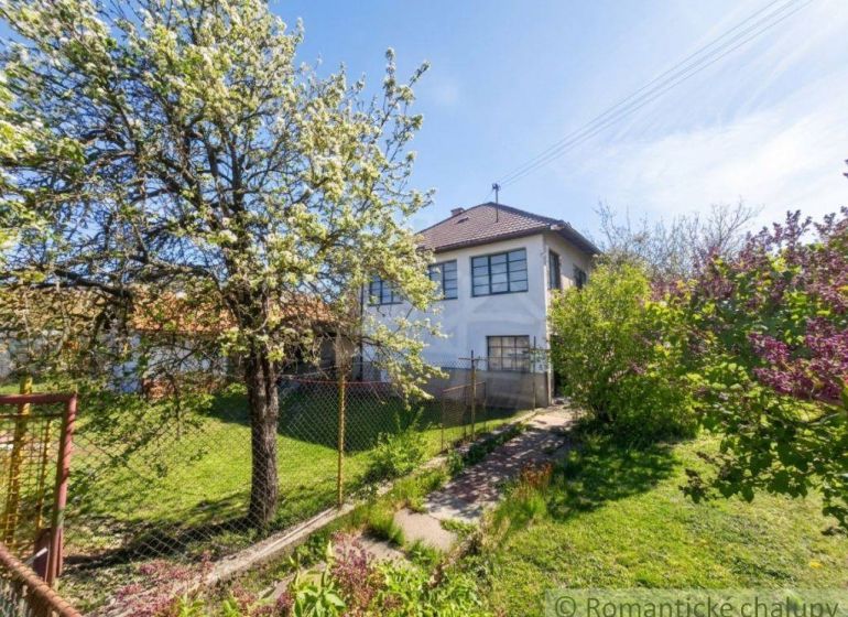 A blooming tree by a family house in Kriváň with a landscaped garden and a fence.
