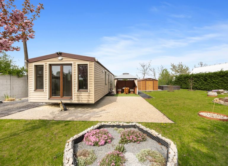 A cottage in Hurbanovo with a blooming garden, a gazebo, and a gravel path.