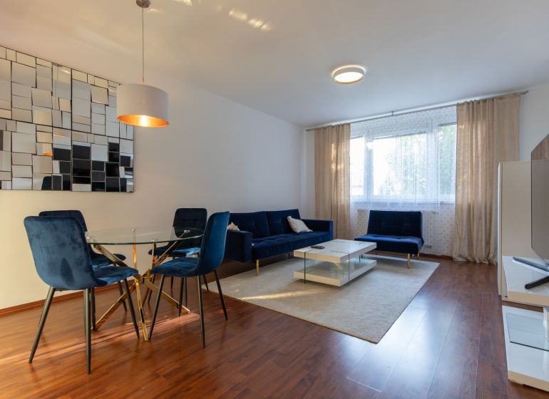 Living room in a two-room apartment with blue chairs and wood-patterned flooring.