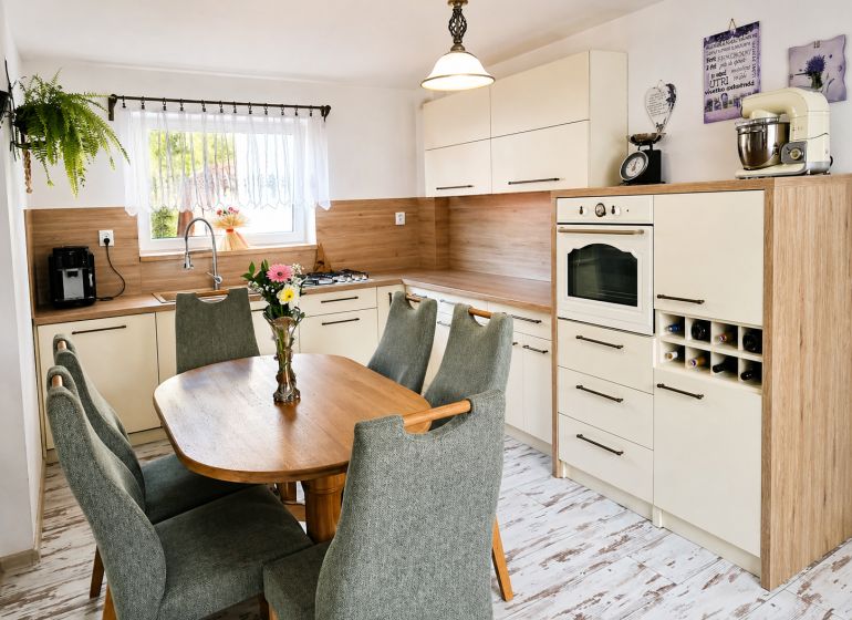 A kitchen in a family house with wooden decor, green chairs, a dining table, appliances.