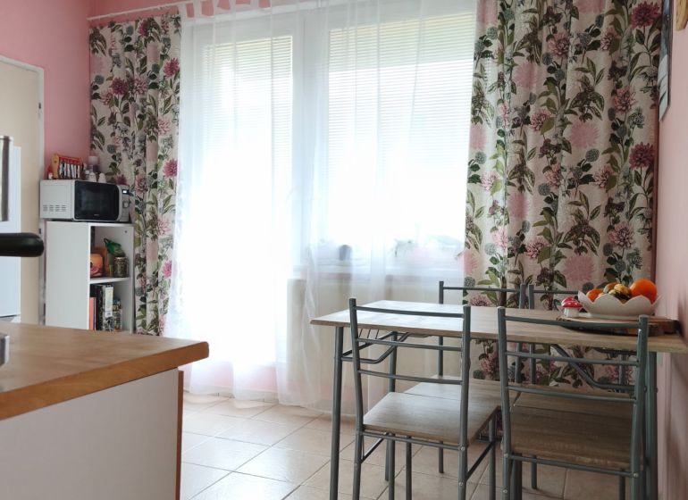 Dining area in a 2-room apartment with a table and floral curtains.