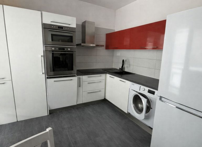 The kitchen of a 4-room apartment with an L-shaped kitchen unit, an oven, and a washing machine.