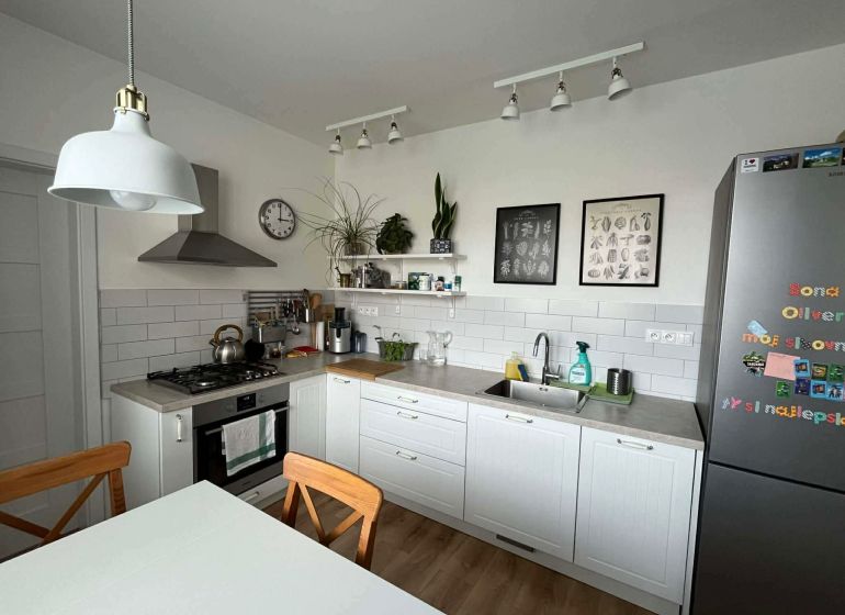 A kitchen in a 3-room apartment with white cabinets, a wooden decor floor, and decorations.