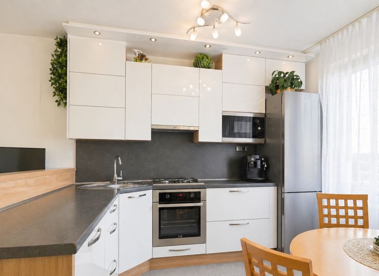 A kitchen in a 3-room apartment with white cabinets, a corner sink, and a dining table.