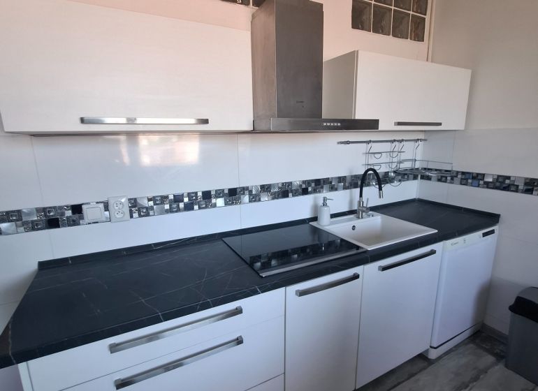 A kitchen in a 3-room apartment with glossy white cabinets and a dark countertop.