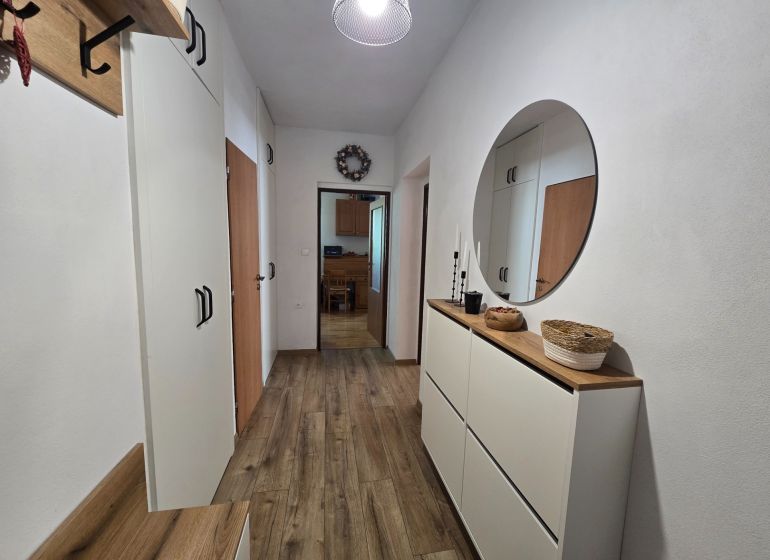 The entrance hall in a 2-room apartment with white furniture and a wooden decor floor.