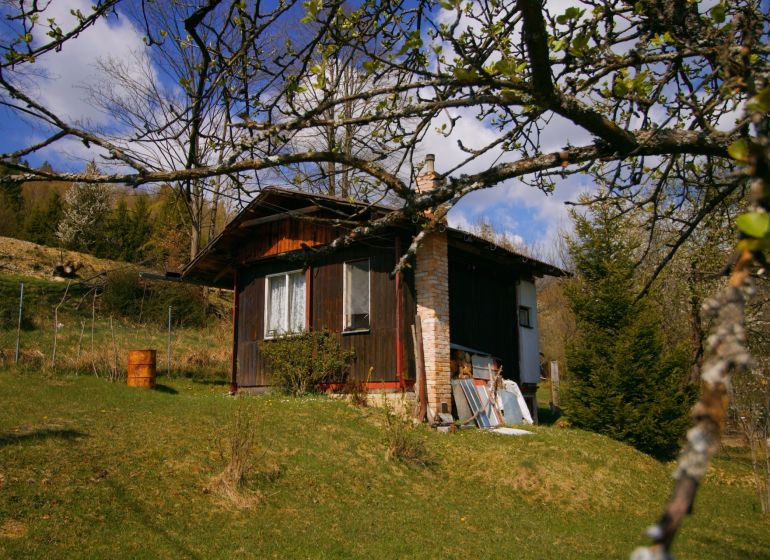 A wooden cottage in Krásno nad Kysucou surrounded by trees and grass on a slope.