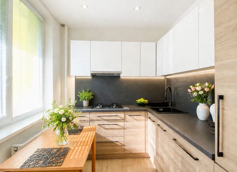 A kitchen in a 2-room apartment with a wooden decor floor and white cabinets.