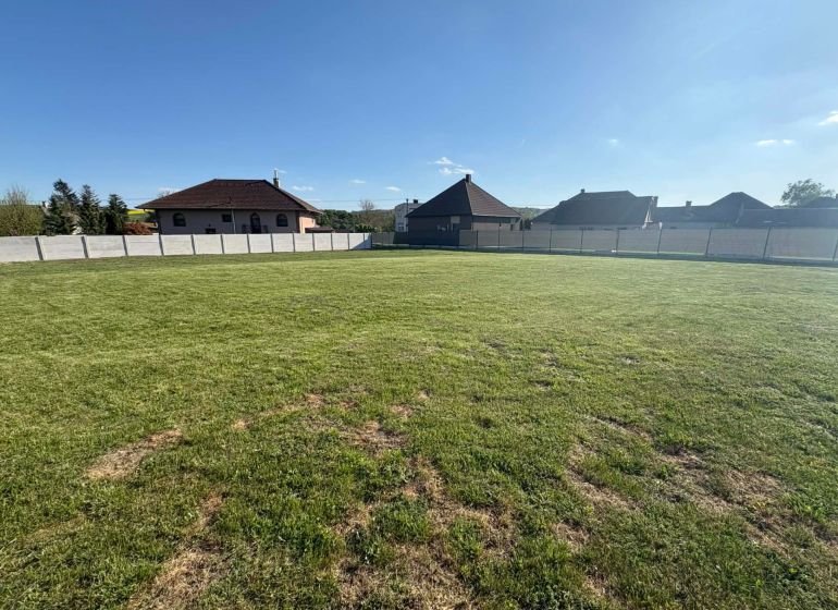 A residential plot in Pozba with a grassy area and surrounding houses.
