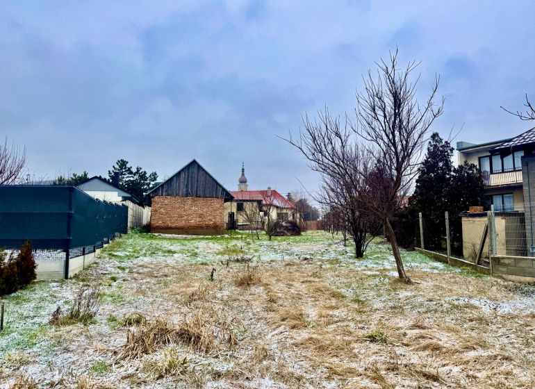 A snowy plot with a house without a facade in Dvorníky, fencing, grassy terrain, blades of grass.