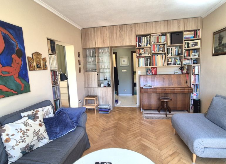 Living room in a two-room apartment with a piano, sofas, and a wooden decor floor.