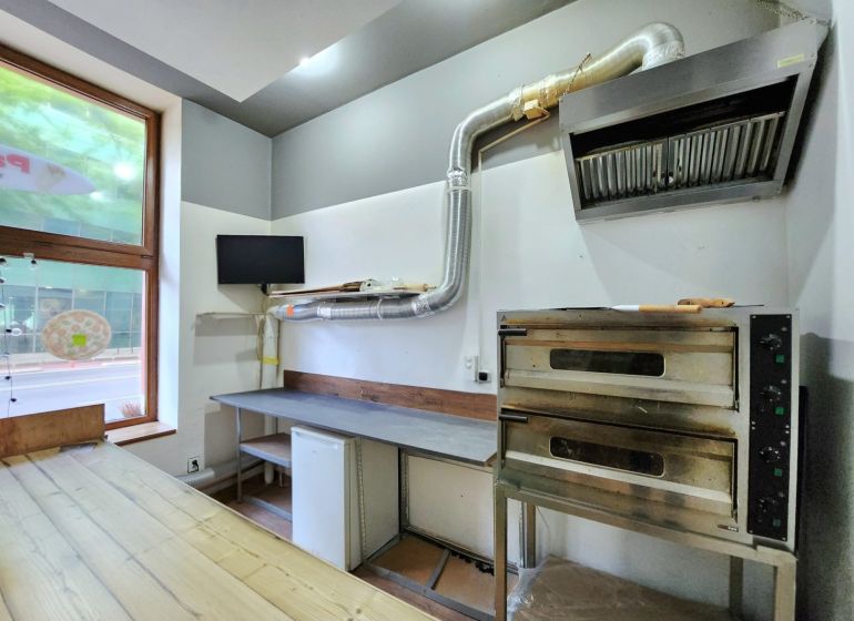 A bakery oven and a table with a hood in a gastro space on a floor with a wooden decor.