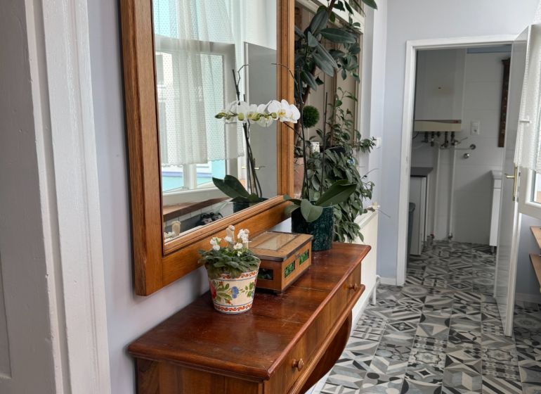 Wooden dresser with flowers and a mirror, designed tiles on the floor.
