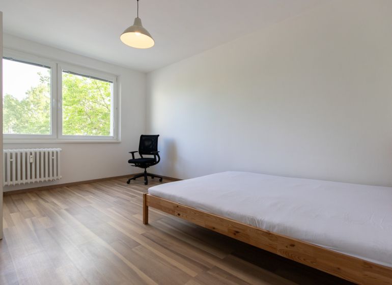 Bright bedroom in a 3-room apartment with wood-patterned flooring and large windows.
