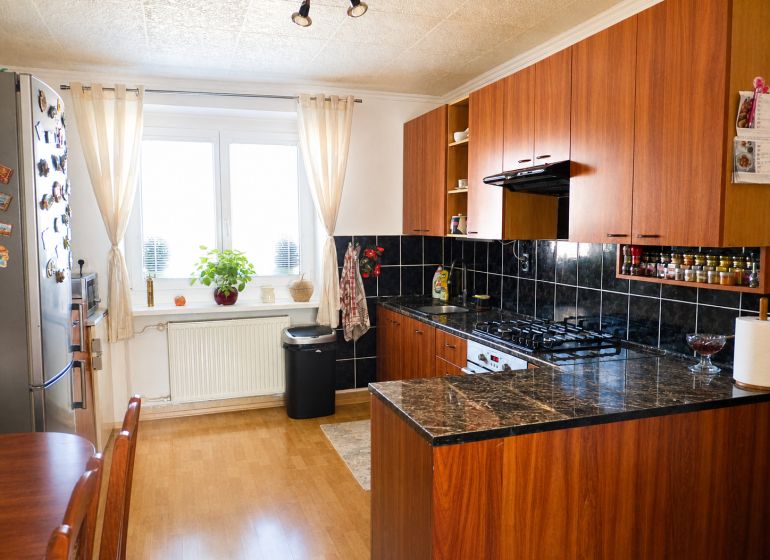 A kitchen in a 2-room apartment with a wooden decor floor and dark tiles.