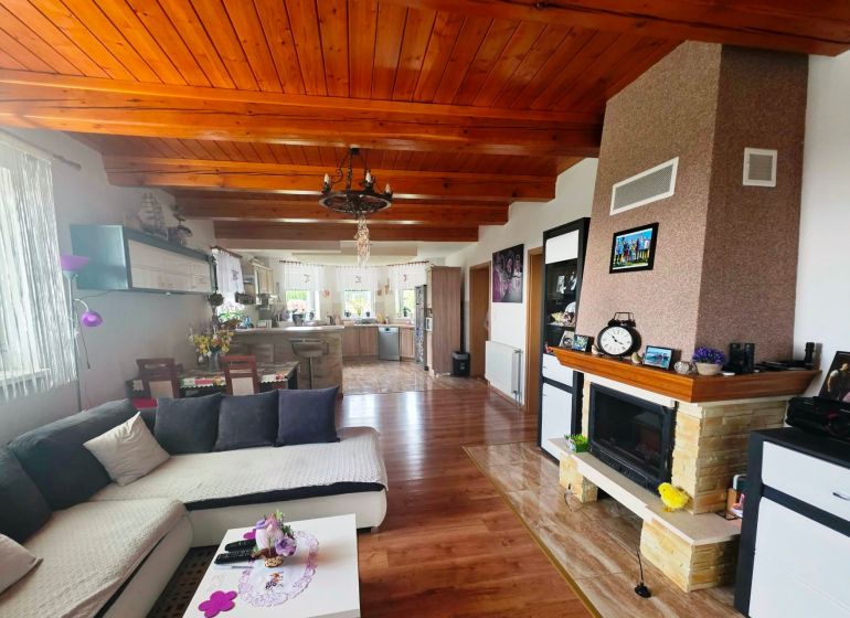 Living room with kitchen, fireplace, and wooden decor flooring in a family house.