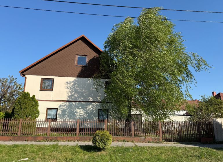 A family house in Zlaté Moravce, a garden with trees, a fence, and a blue sky.