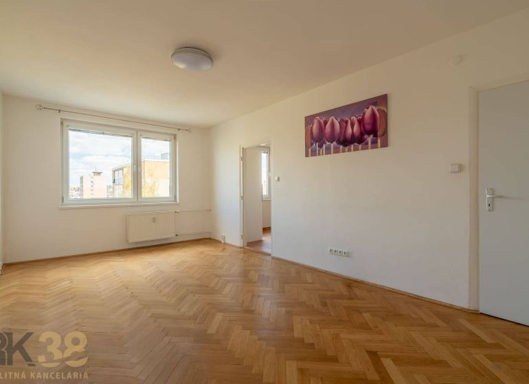 A spacious room with a large window, wooden decor flooring, and a painting in a 4-room apartment.