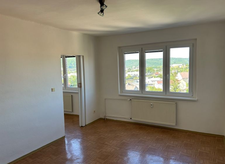 A bright room with three windows and a wooden decor floor in a two-room apartment.