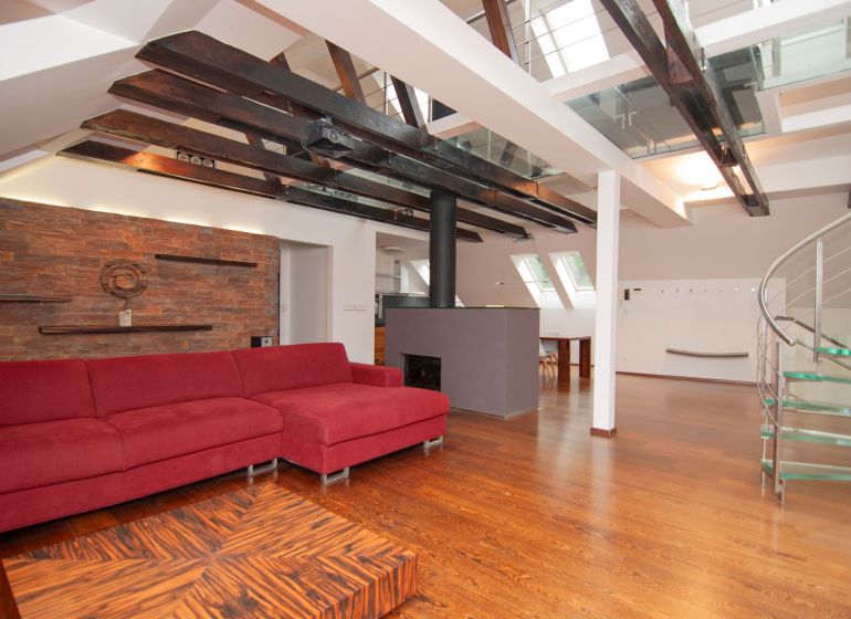 Attic living space with a large red sofa and wood-patterned flooring in a 3-room apartment.