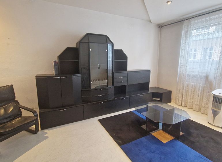Living room with a sofa, glass table, and dark wall unit in a 3-room apartment.