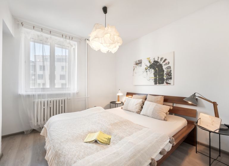 A bright bedroom with a wooden bed, a painting on the wall, and a floor with a wooden decor.