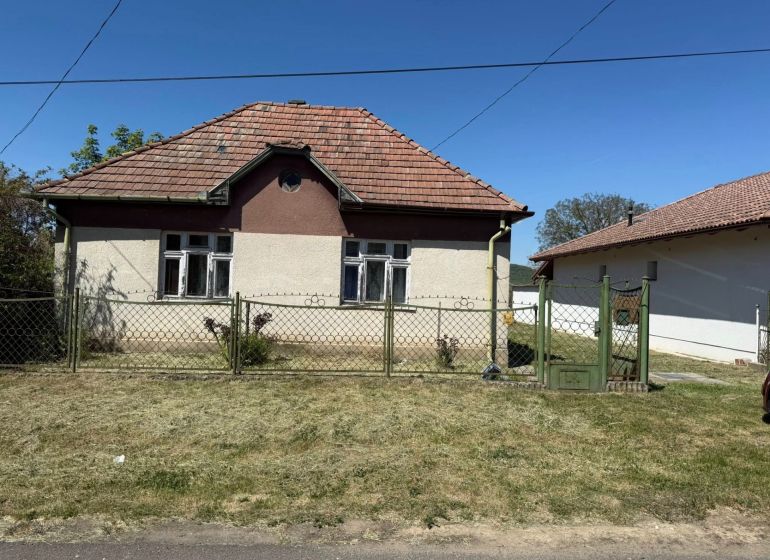 A family house in Hont has a sloped roof and is enclosed by a metal fence.