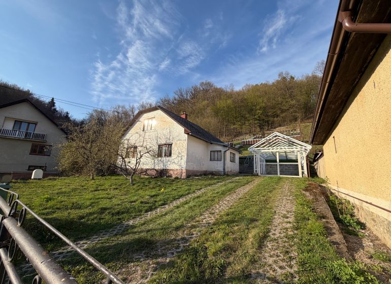 A family house in Štós surrounded by greenery and a wooden structure of a shelter.