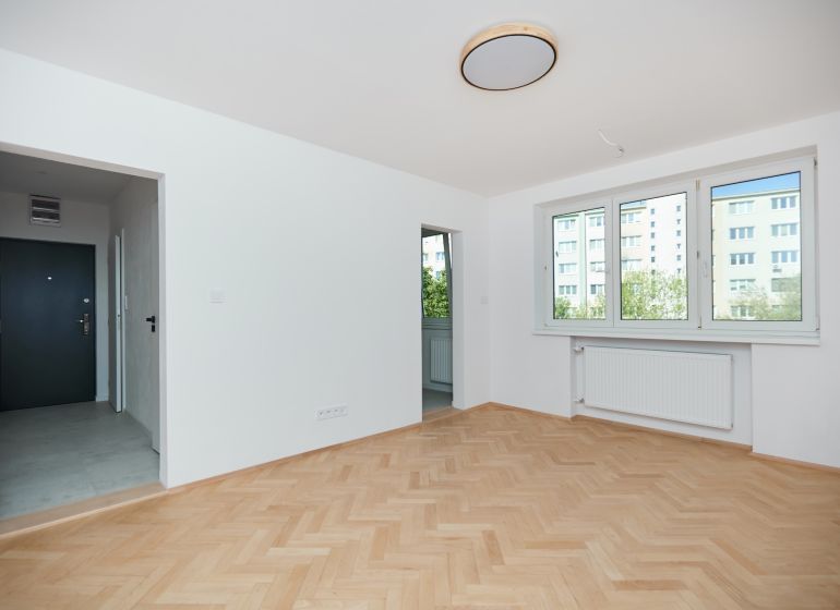 An apartment with a wooden floor design, white walls, and large windows.